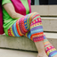 A woman sitting on stairs in She's Got Leggz leggings called Rainbow Connections. They are colorful, striped, and have circles and lines on them.